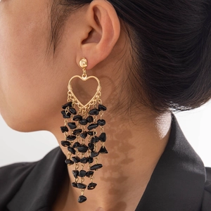 Close-up of heart-shaped tassel earrings with black stones and gold metal finish