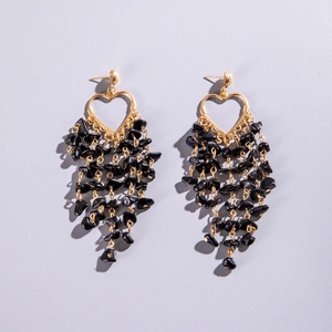 Close-up of golden hollow heart earrings with dangling black natural stone tassels