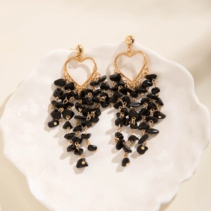 Close-up of heart-shaped gold earrings with dangling black stone tassel fringe