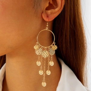 Detail of bohemian gold tassel earrings featuring textured discs on a female model