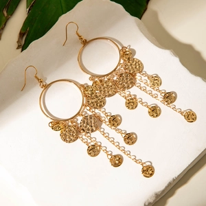Close-up of golden U-shaped tassel earrings with hammered discs on stone texture