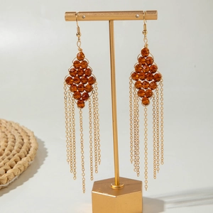 Detail of amber glass bead earrings with golden fringe tassels on a display stand