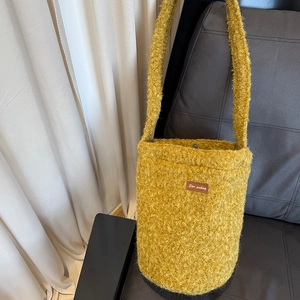 Macro detail of plush yellow fleece texture and leather logo on the shoulder bucket bag