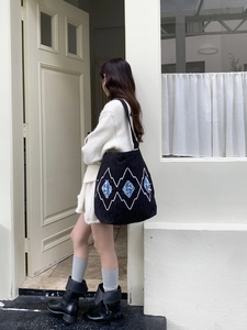 Detail of black tote bag featuring white wavy embroidery and light blue diamond patches
