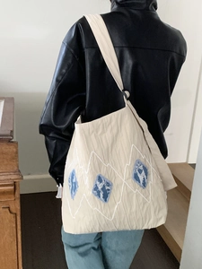 Detail of beige canvas shoulder bag with blue diamond patches and wave stitching