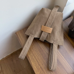 Detail of tan suede tote bag featuring a stitched leather tag with embossed typography