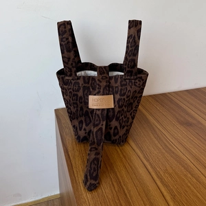 Detail of leopard print canvas tote bag featuring brown leather patch and dual handles
