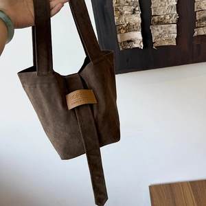 Detail of dark brown suede tote bag featuring unique leather patch and contrast stitching