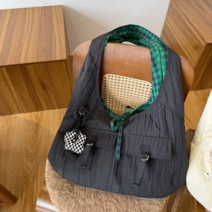 Detailed view of black quilted nylon tote bag with green plaid lining on a wooden chair