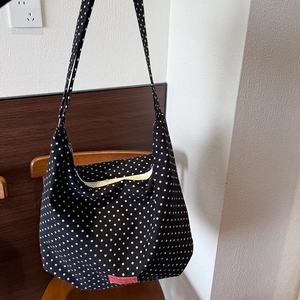 Detailed shot of black canvas bag with white polka dots and red label on wooden chair