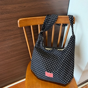 Detailed close-up of a black canvas tote bag with white polka dots and red woven label