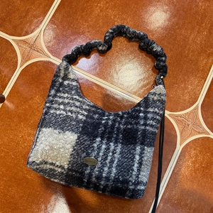 Detail of checkered plush tote bag featuring handmade metal logo and ruched handle texture