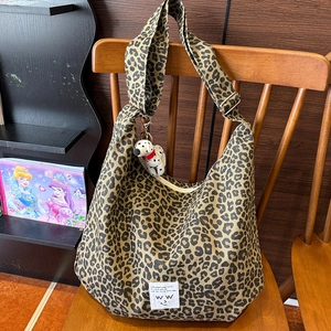Leopard print canvas shoulder bag with a cute dalmatian plush keychain on a wooden chair