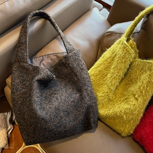 Borse tote invernali in tweed marrone e peluche giallo su divano in pelle nera