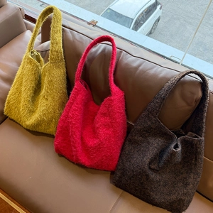 Borse tote invernali in peluche nei colori giallo, rosso e marrone scuro sul divano