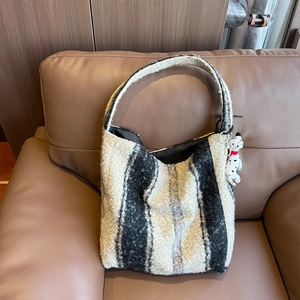 Dettaglio borsa tote a righe in pile morbido con ciondolo a forma di dalmata sul divano