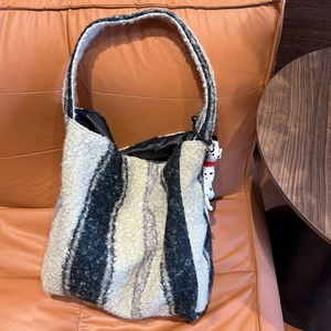 Dettaglio di una borsa tote in pile a righe con ciondolo a forma di cane sul divano