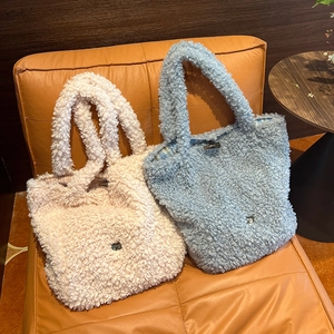 Detail of curly faux fur tote bags with toggle button closure and metal logo on orange leather