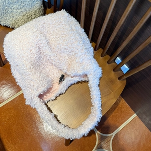 Detail of pink faux shearling tote bag with black toggle closure on a wooden chair