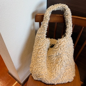 Detailed texture of a beige teddy fleece tote bag on a rustic wooden chair backdrop
