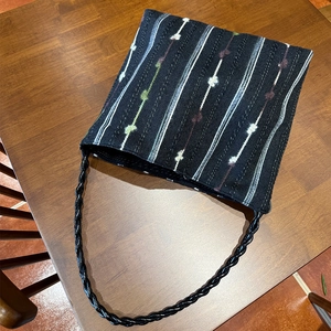 Detail of colorful striped knitted shoulder bag with woven rope strap on wooden desk