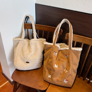 Vue détaillée de sacs cabas en peluche avec broderie sur une chaise en bois