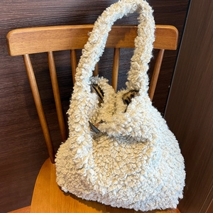 Chic beige faux shearling tote bag with horn clasp on a wooden chair setting