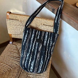 Detail of hand-woven striped texture and leather logo patch on a knit crossbody bag