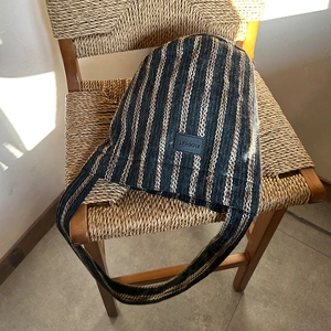 Close-up of a striped knit crossbody bag showing thick woven texture and leather logo tag