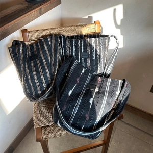 Handmade woven striped tote bag in various colors displayed on a vintage wicker chair