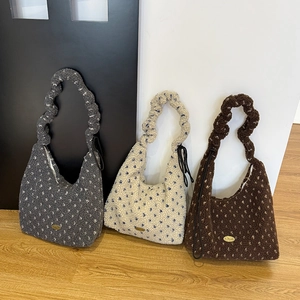 Detail view of plush drawstring bags in grey, white and brown with gold branding plaques