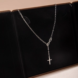 Macro detail of silver infinity cross necklace on a premium black velvet jewelry box