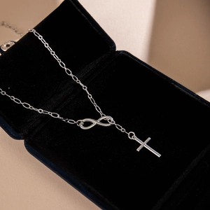 Detail of silver infinity and cross pendant necklace resting on a blue velvet jewelry box