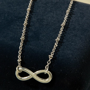 Macro shot of silver infinity symbol pendant necklace on blue velvet display stand