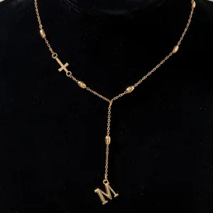 Detail of gold Y-shaped necklace with cross element and dangling letter M pendant