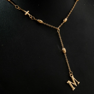 Detailed shot of gold layered necklace with letter M pendant and small cross charm
