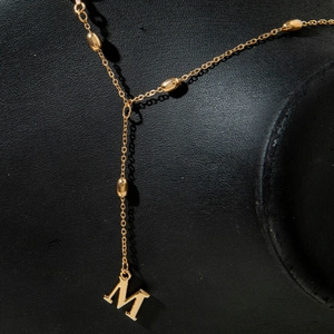 Close-up of a gold-plated necklace featuring a large letter M pendant on a black stand