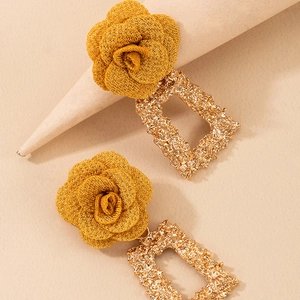 Détail de boucles d'oreilles rose en tissu jaune avec pendentifs dorés rectangulaires