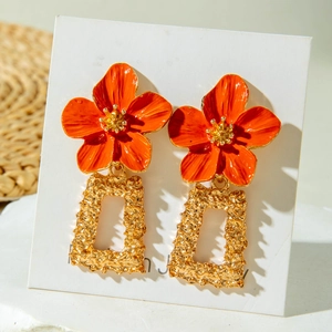 Détail de boucles d'oreilles fleurs orange avec pendentifs dorés texture lave