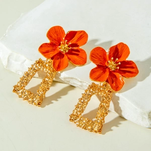 Détail de boucles d'oreilles pendantes vintage dorées avec fleurs orange et texture métal