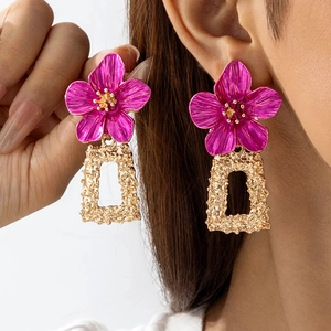 Gros plan sur les boucles d'oreilles fleurs rose fuchsia et cadres dorés martelés