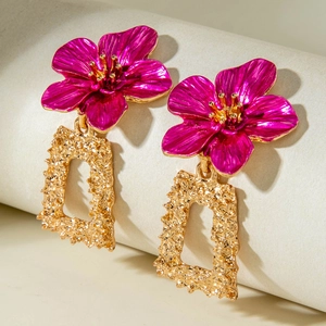 Détail de boucles d'oreilles fleur en métal rose sur un cadre rectangulaire doré