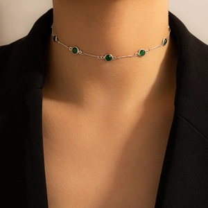 Detalle de un collar con piedras esmeralda verdes en una modelo con chaqueta negra