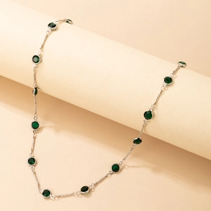 Detalle de collar de plata con piedras esmeralda verdes sobre un soporte minimalista beige