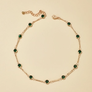 Detalle de collar dorado con cristales verde esmeralda y cierre de mosquetón ajustable