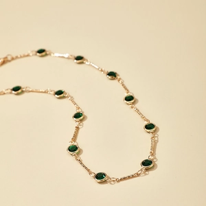 Primer plano de collar de cadena dorada con múltiples gemas verdes redondas y fondo beige