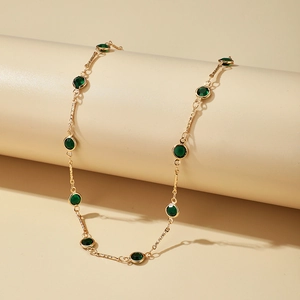 Detalle del collar dorado con piedras preciosas verdes y eslabones en el expositor