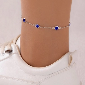 Primer plano de una tobillera plateada con cristales azules y zapatillas blancas