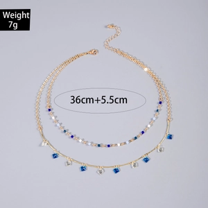 Detalle de collar doble dorado con cuentas azules y colgantes de cubo, largo 36+5,5cm