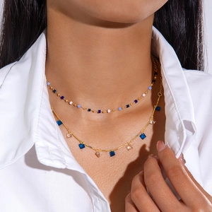 Primer plano de collar dorado a capas con cristales cuadrados azules sobre camisa blanca